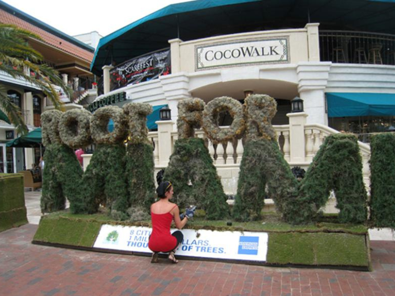 Woman in front of a life-size sign made out of moss. 